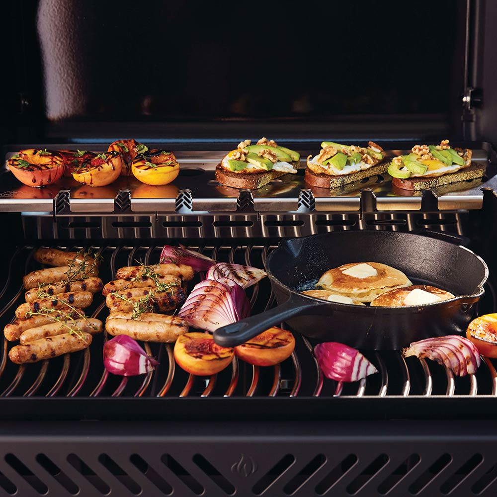 Black gas grill interior with grilled vegetables, burgers, and sausages