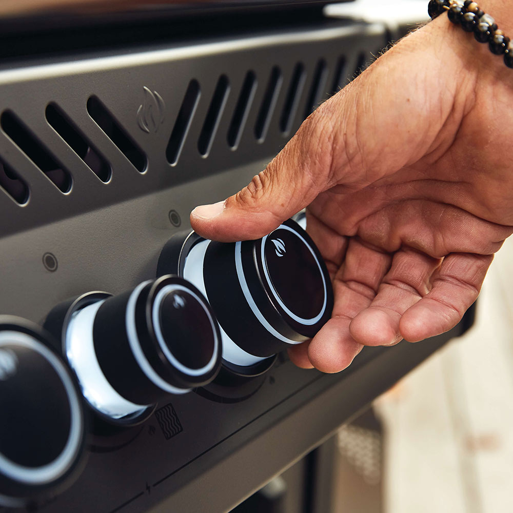 Close-up of hand turning a gas grill control knob on the front panel