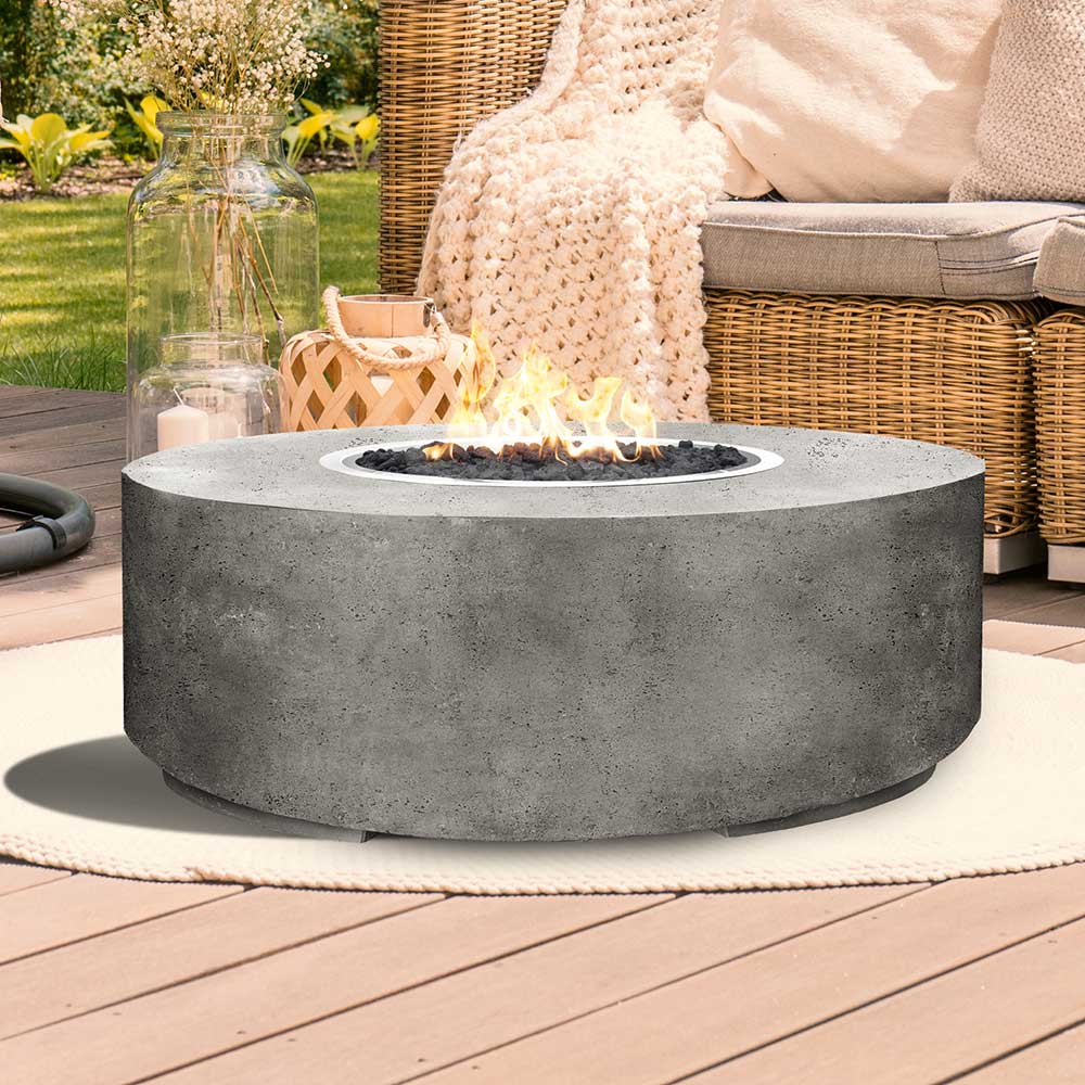 Round concrete gas fire pit with flames, light gray finish on patio