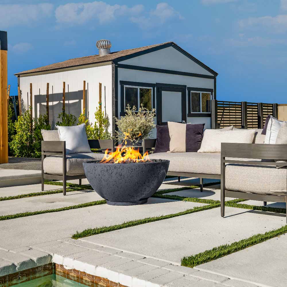Gas fire bowl with flames, dark gray stone finish on outdoor patio