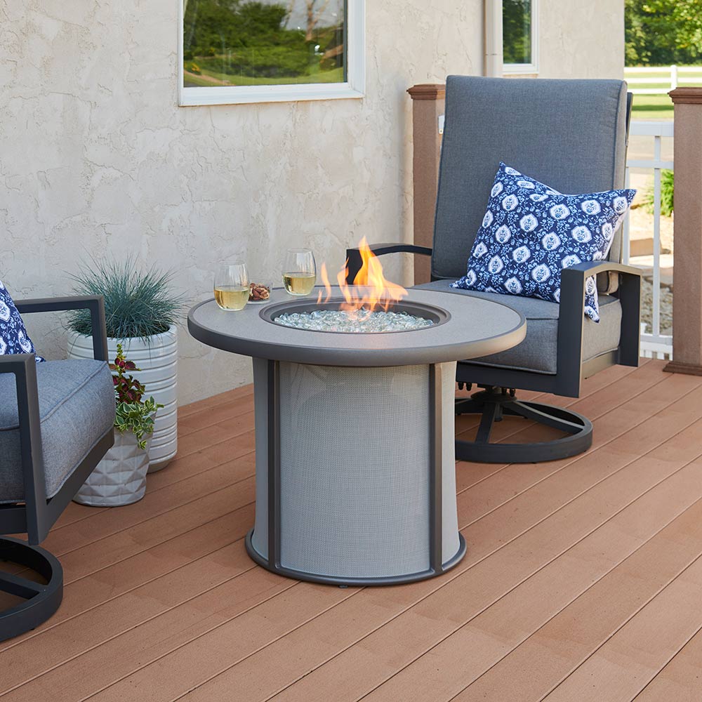 Round gray gas fire table with flames in center and mesh fire surround