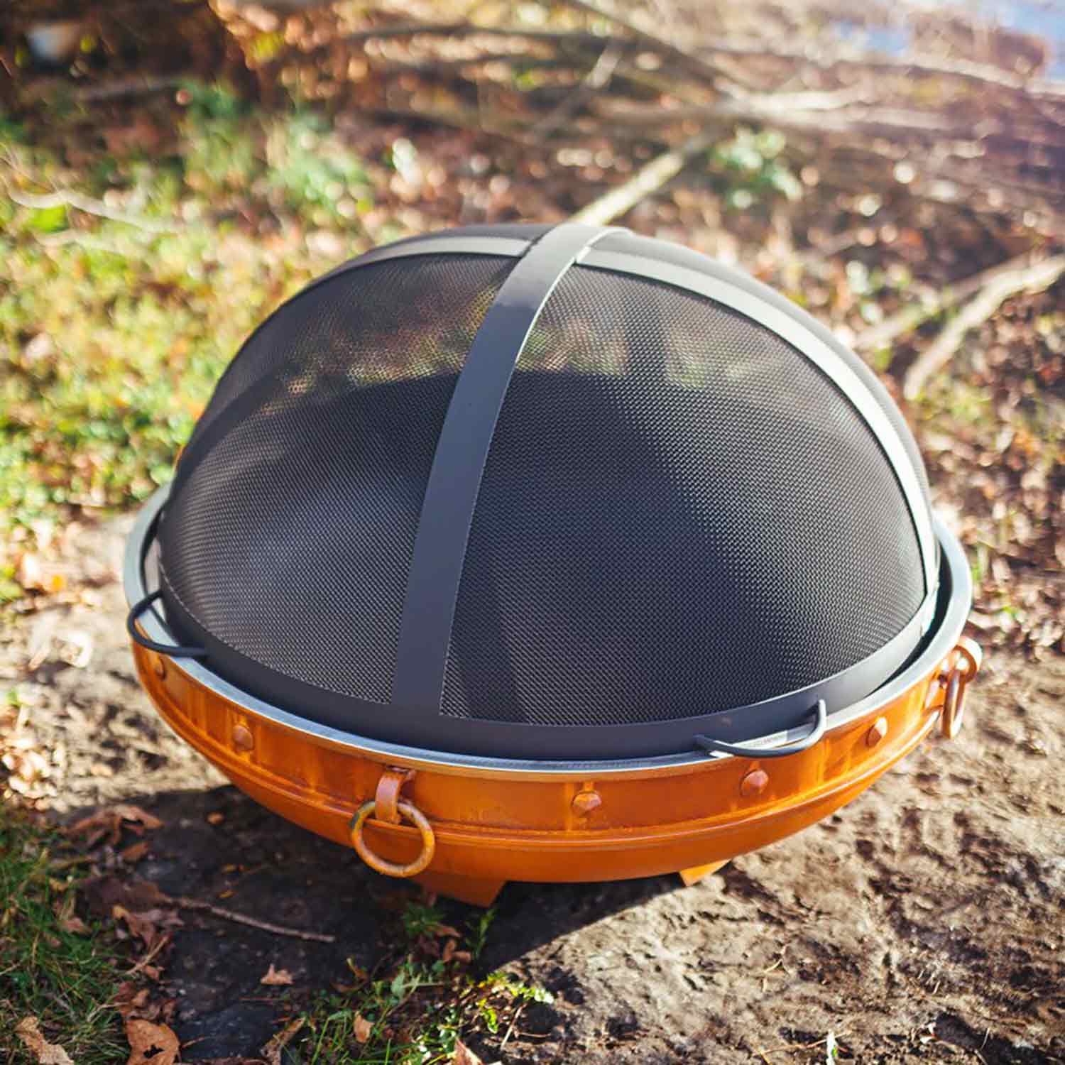 Fire pit spark guard with black mesh dome and silver rim ring over orange bowl