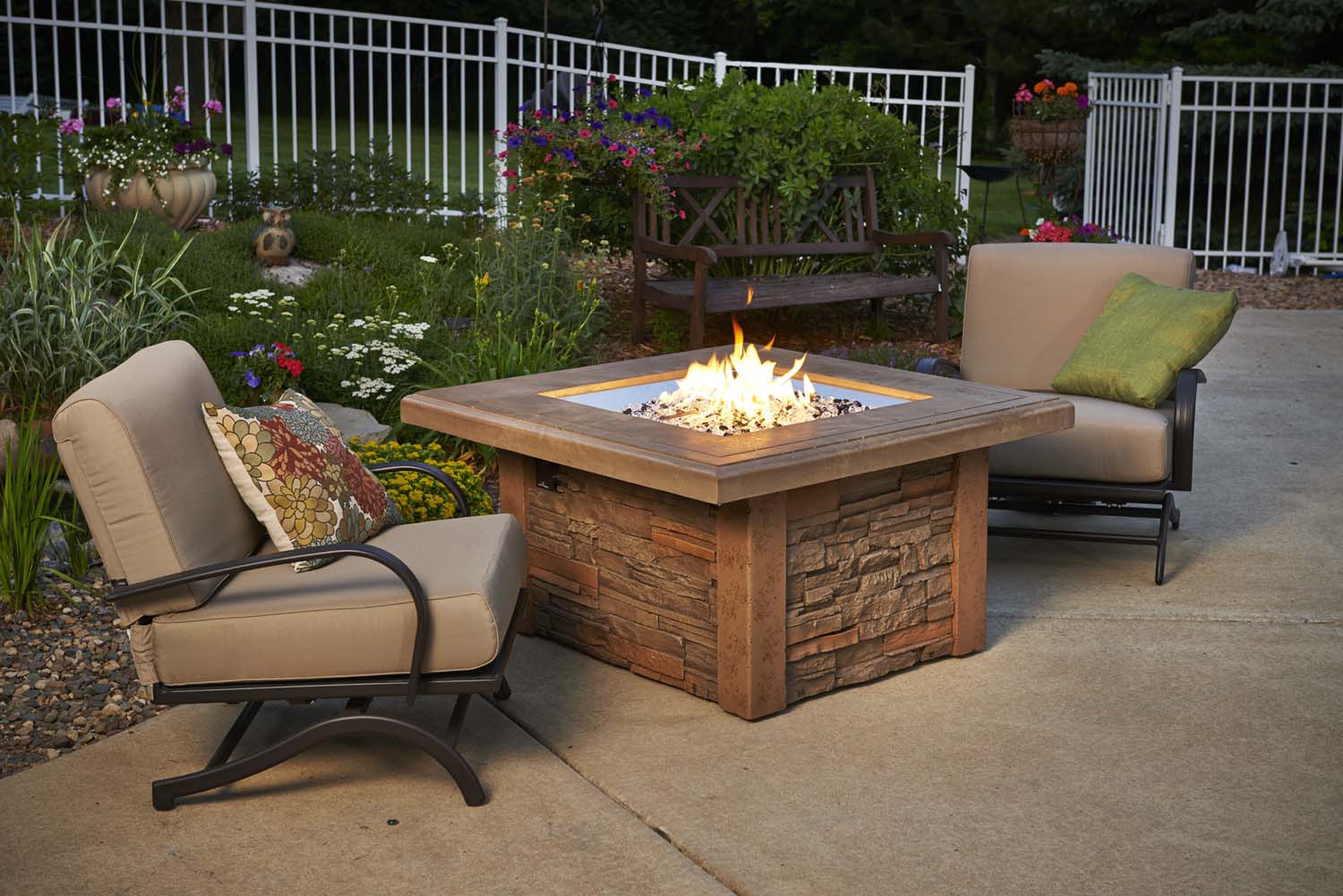 Outdoor square gas fire table with stone base, tan tabletop, and visible flames