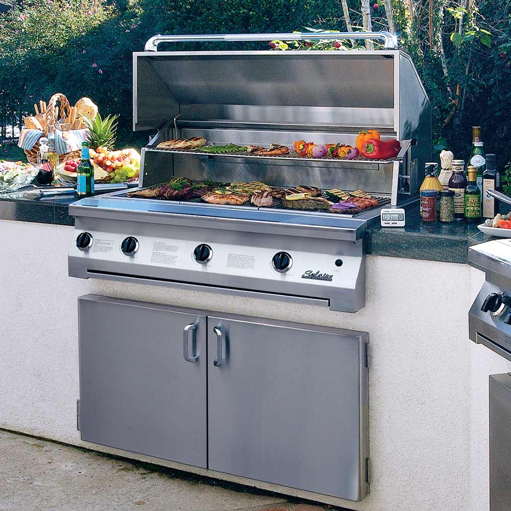Outdoor stainless built-in grill with open lid and food on searing grates.