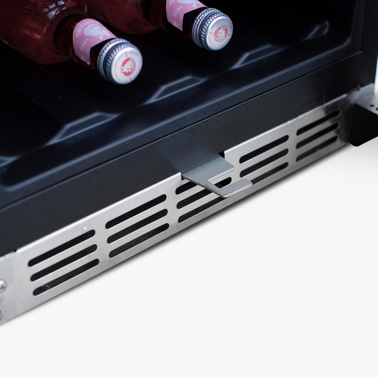 Bottom interior shelf of refrigerator with front vented grille and bottled drinks