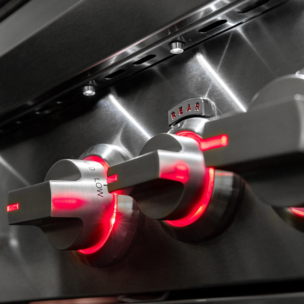Gas grill control knobs with red indicator lights in the firebox area