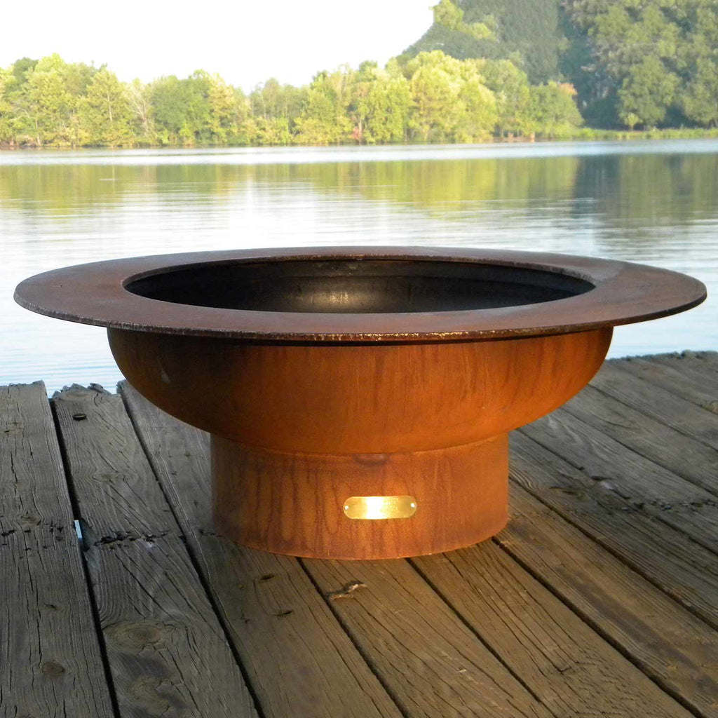 Round gas fire pit with open center and rust-brown body on wooden deck