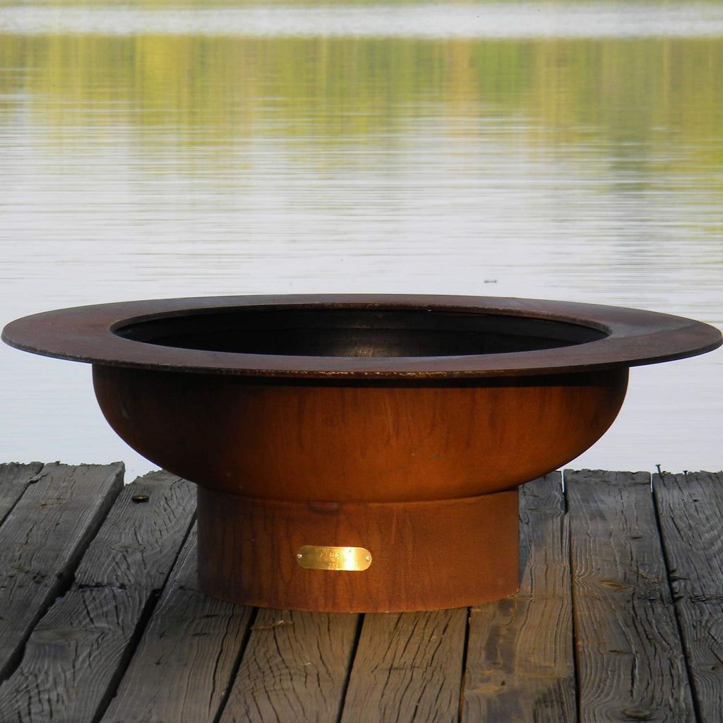 Round gas fire pit with dark top ring and rust-colored metal body with ignition window
