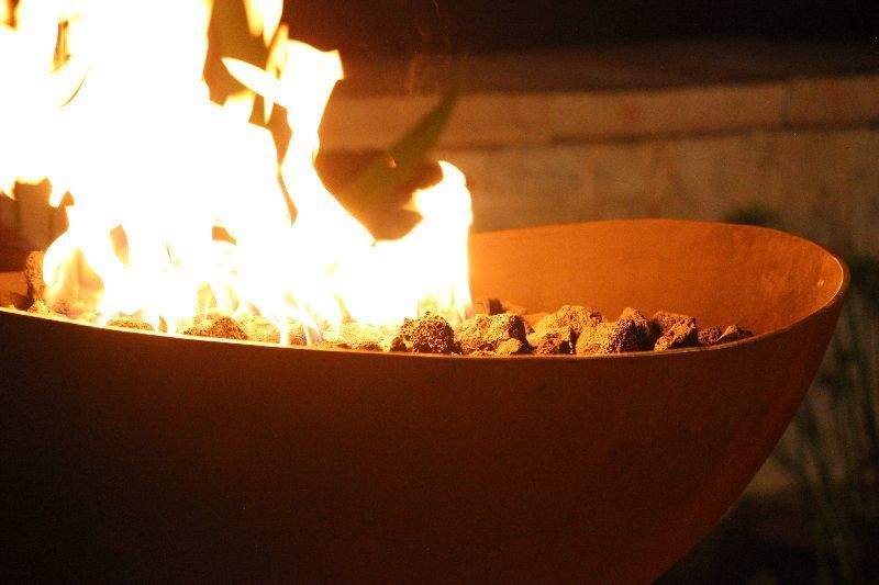 Close-up of burning gas fire pit bowl with bright flames over rock bed.