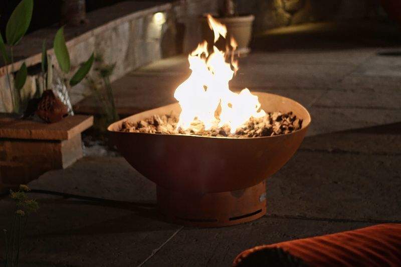 Burning gas fire pit with round metal bowl and rock-filled burner grate.