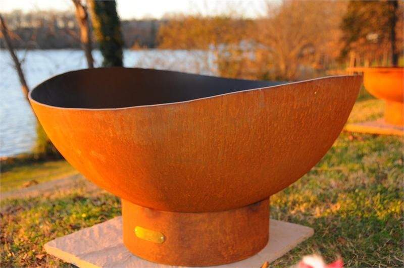 Rust-orange gas fire pit bowl with black interior and round pedestal stand.