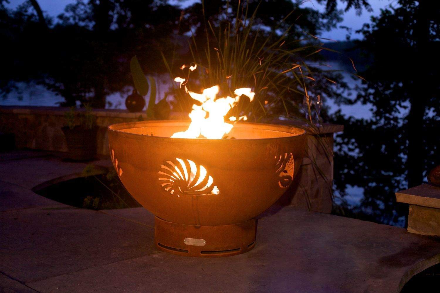 Gas fire pit bowl with sea-creature fan cutout, flames burning on outdoor patio