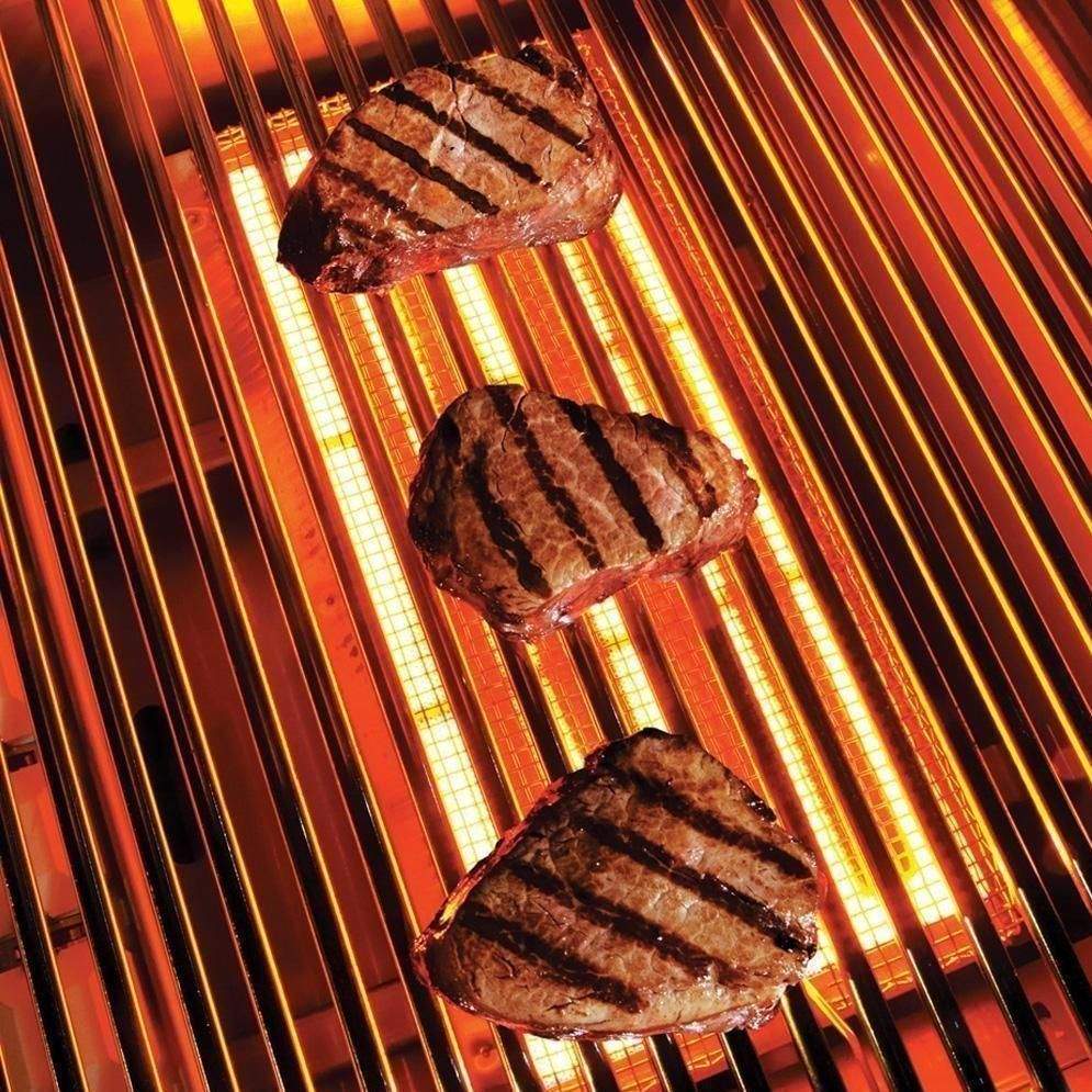 Grilling steaks on a metal grate with glowing flame strips below