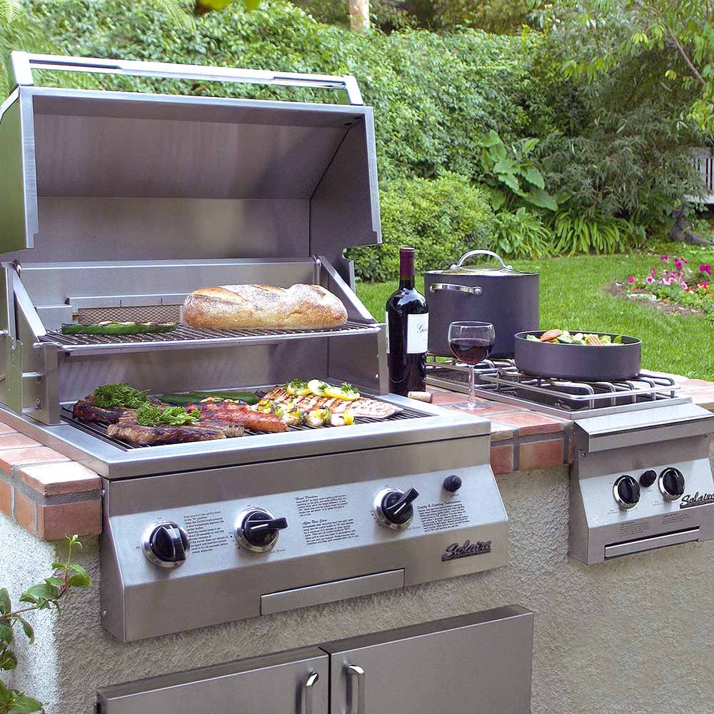 Outdoor built-in gas grill with open lid, cooking grates, and visible food