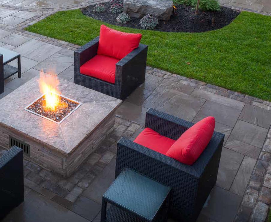 Outdoor fire pit burner producing small flame in a square fire pan
