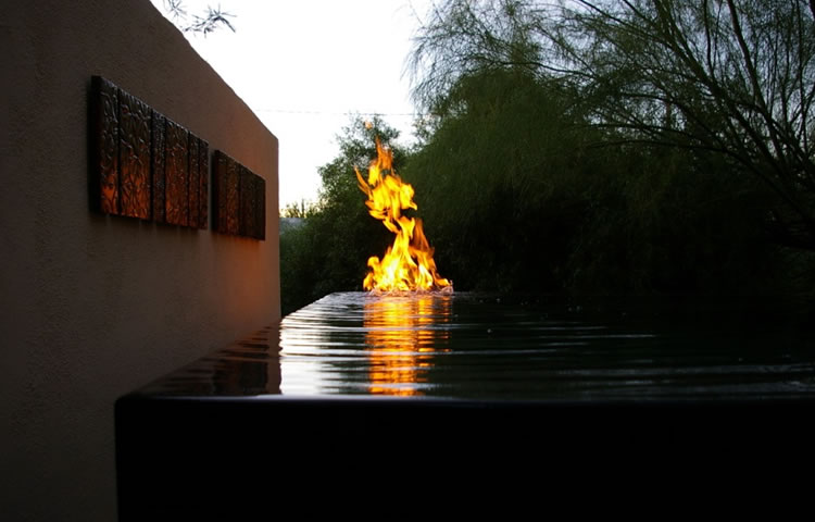 Outdoor gas fire flame rising from pool water near a building wall
