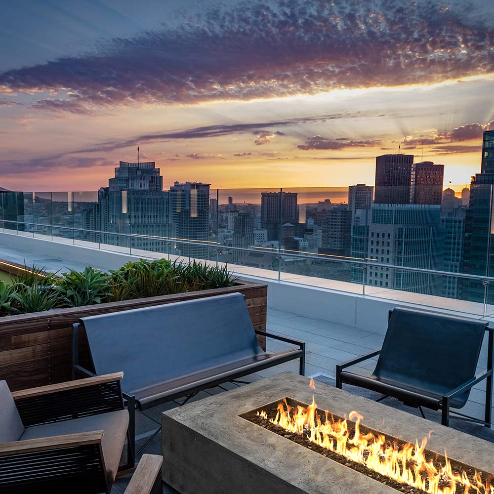 Outdoor concrete gas fire pit with flames and two lounge chairs around it