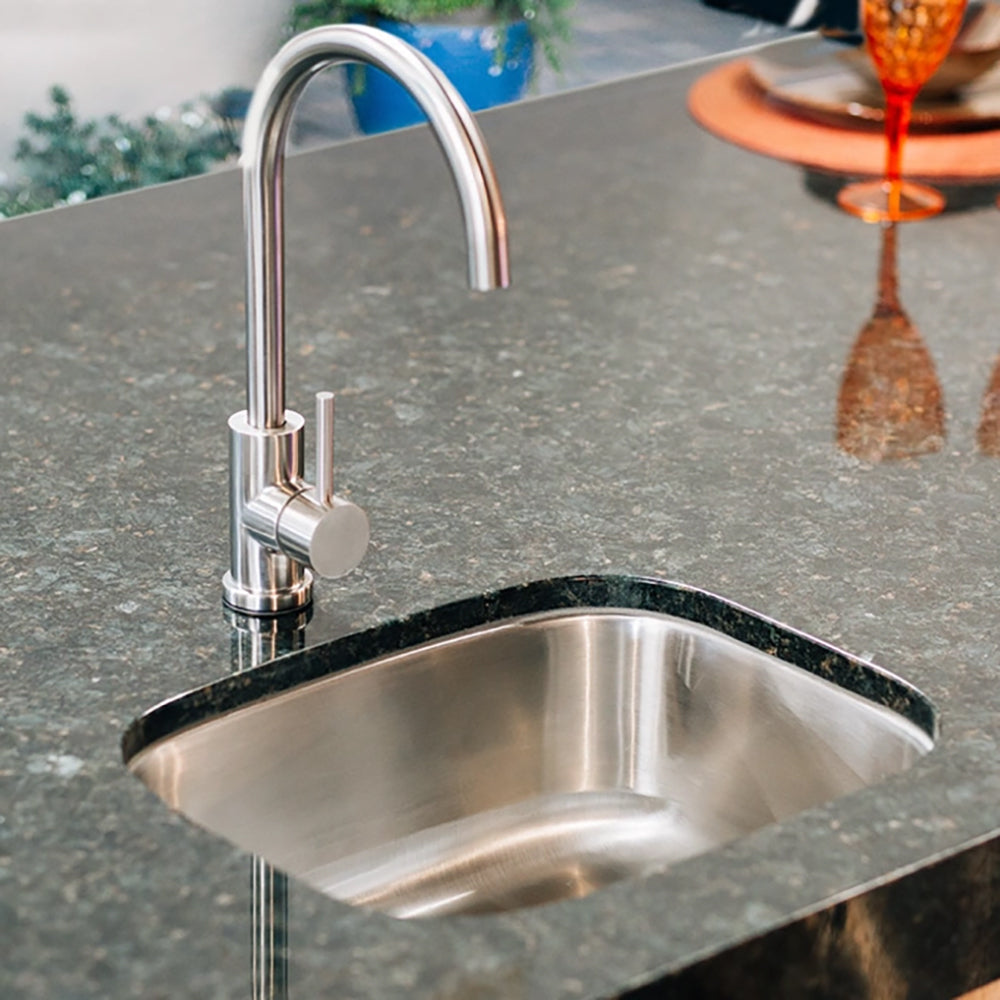 Stainless steel undermount sink with curved faucet mounted on stone countertop