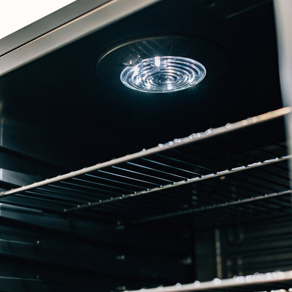 Ceiling light inside outdoor mini fridge above wire shelves and black interior.