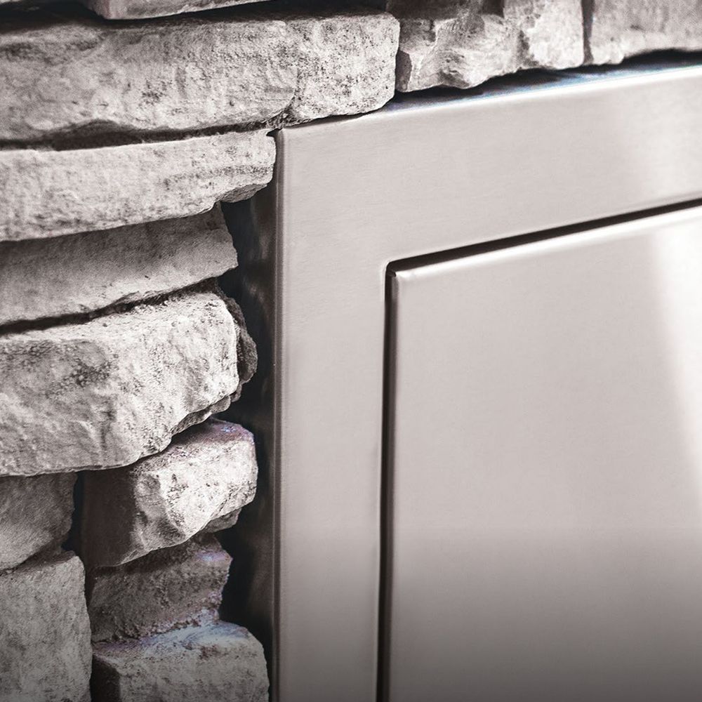 Narrow trash drawer frame beside stone wall, brushed metal finish