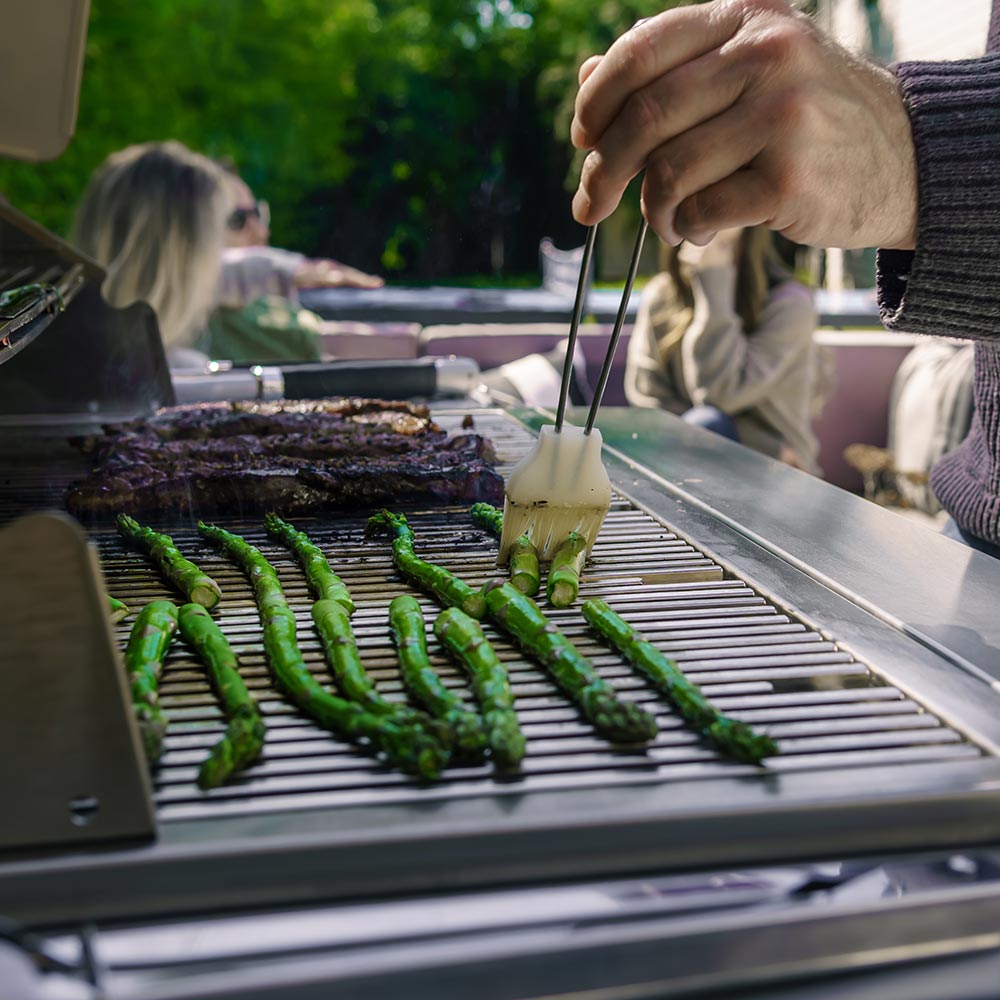 Gas grill cooking grate with grilled vegetables and utensil held over the surface