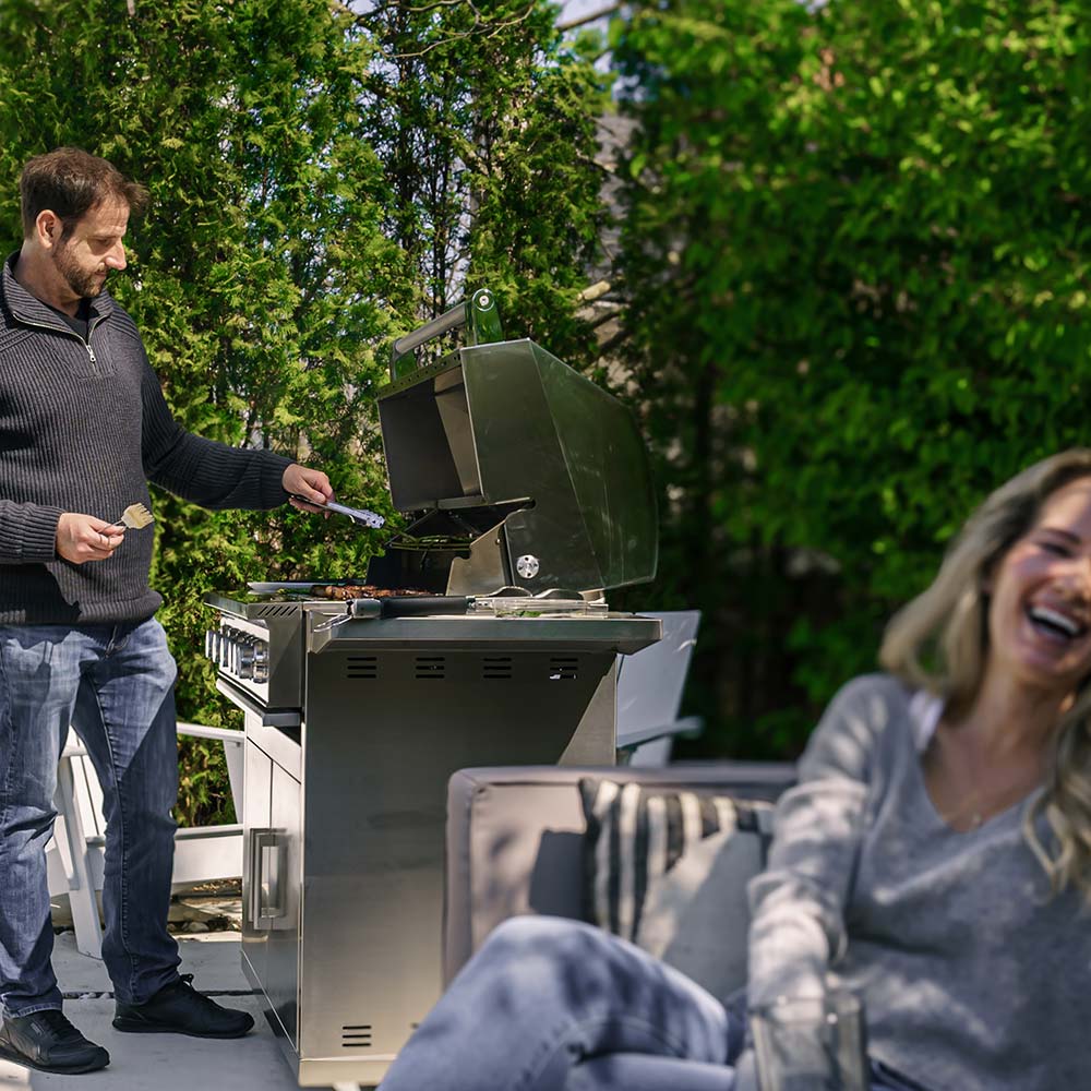 Stainless gas grill with open lid as food is cooked on the main grates