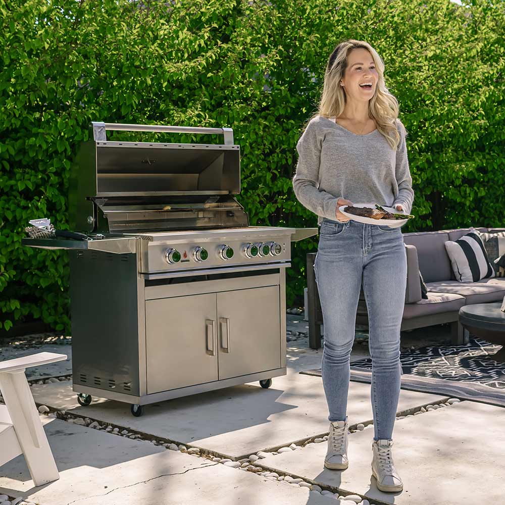 Stainless gas grill with open lid and control knobs beside a standing person