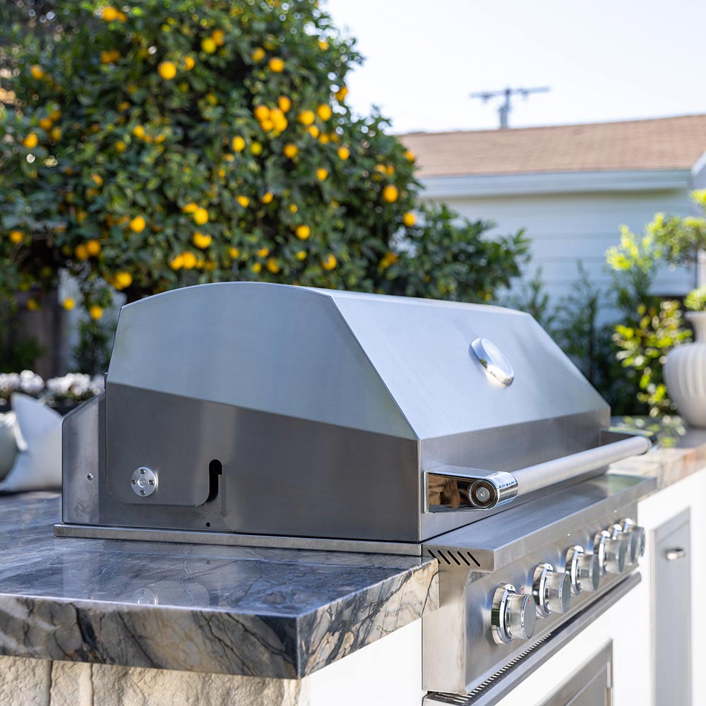 Built-in gas grill with stainless hood and side burner area, showing control controls