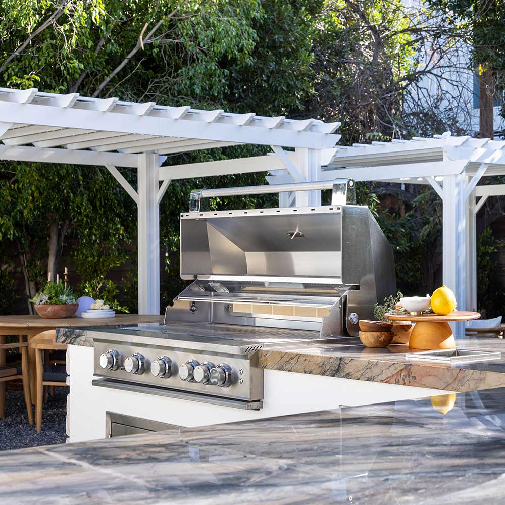 Stainless built-in gas grill with hood and control knobs on outdoor kitchen island