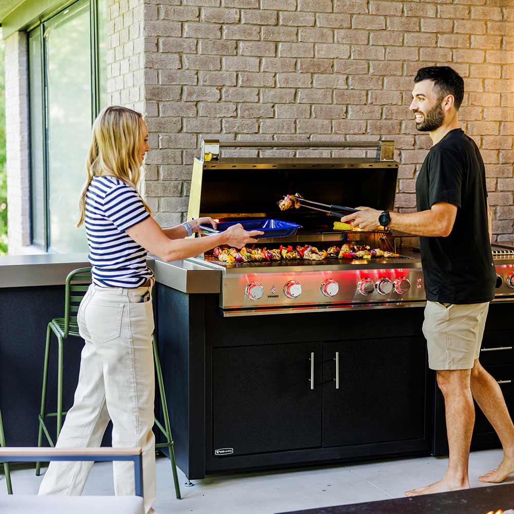 Built-in stainless gas grill with open hood and illuminated burner area, with control knobs