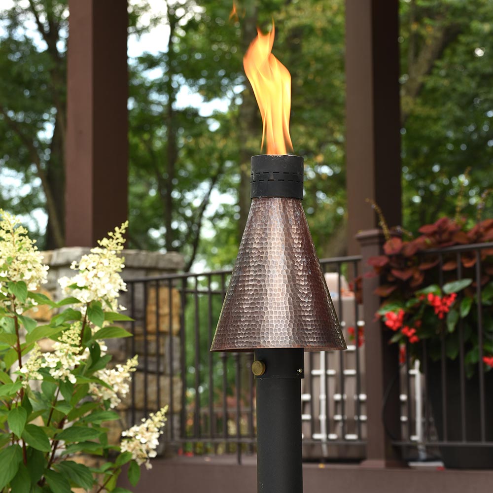 Outdoor gas torch with lit flame and metallic hammered cone on black pole