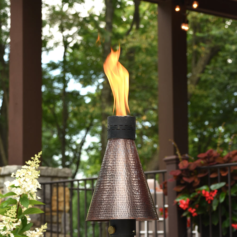 Outdoor gas torch head with hammered copper cone and black burner, lit flame