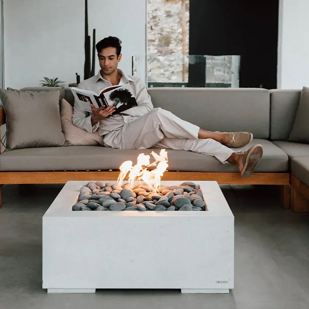 Square concrete gas fire pit with gray stone media and open flames in the basin