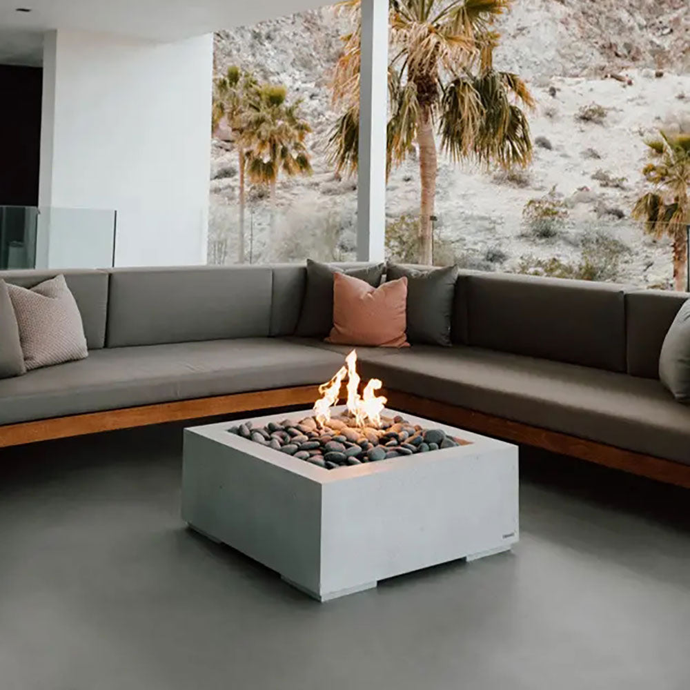 Square concrete gas fire pit with pebble stone bed and flames, centered in the unit