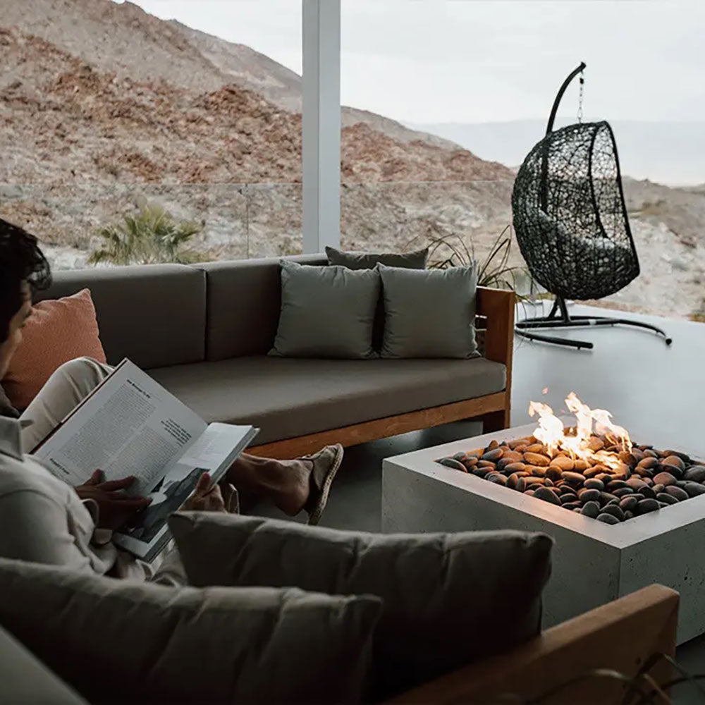Square concrete gas fire pit with pebble stone bed and flames at the top opening