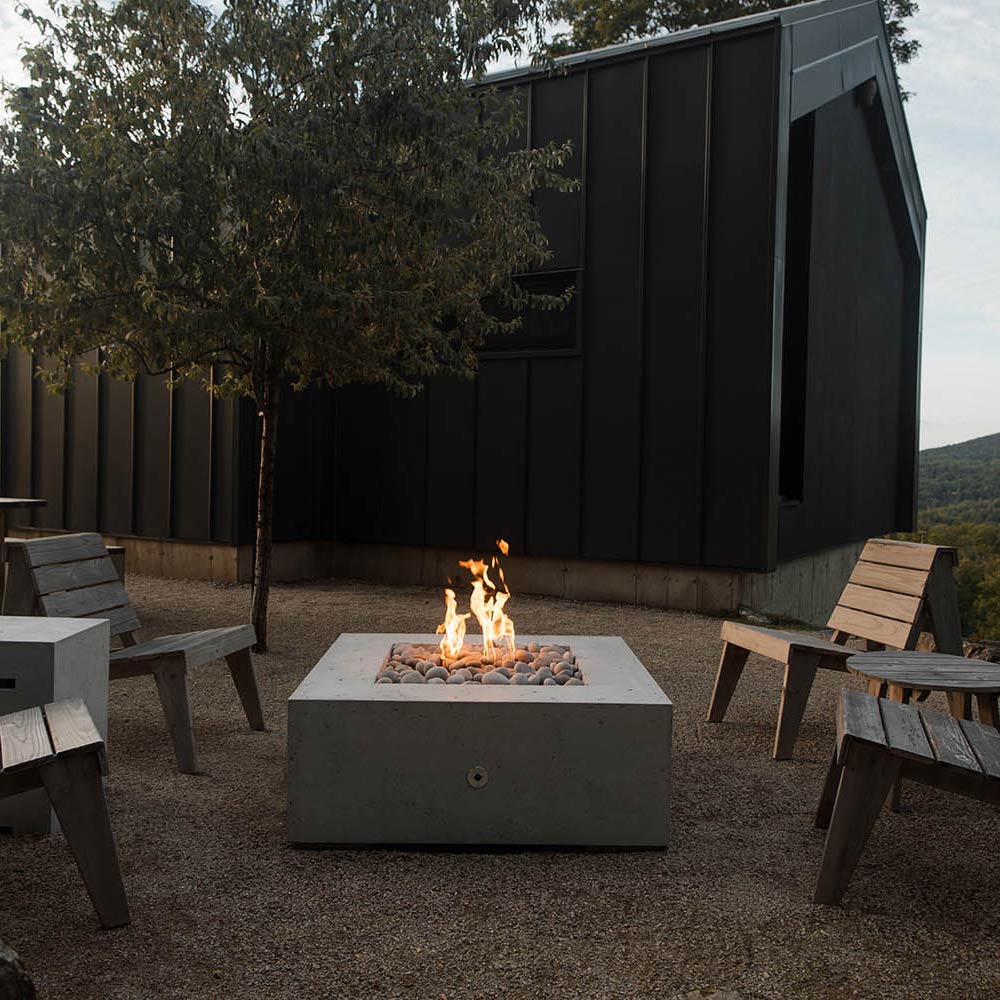 Square concrete gas fire pit with flames in a stone-filled basin