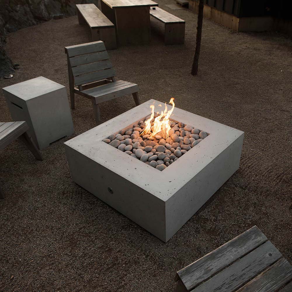 Square concrete gas fire pit with flames over gray stones