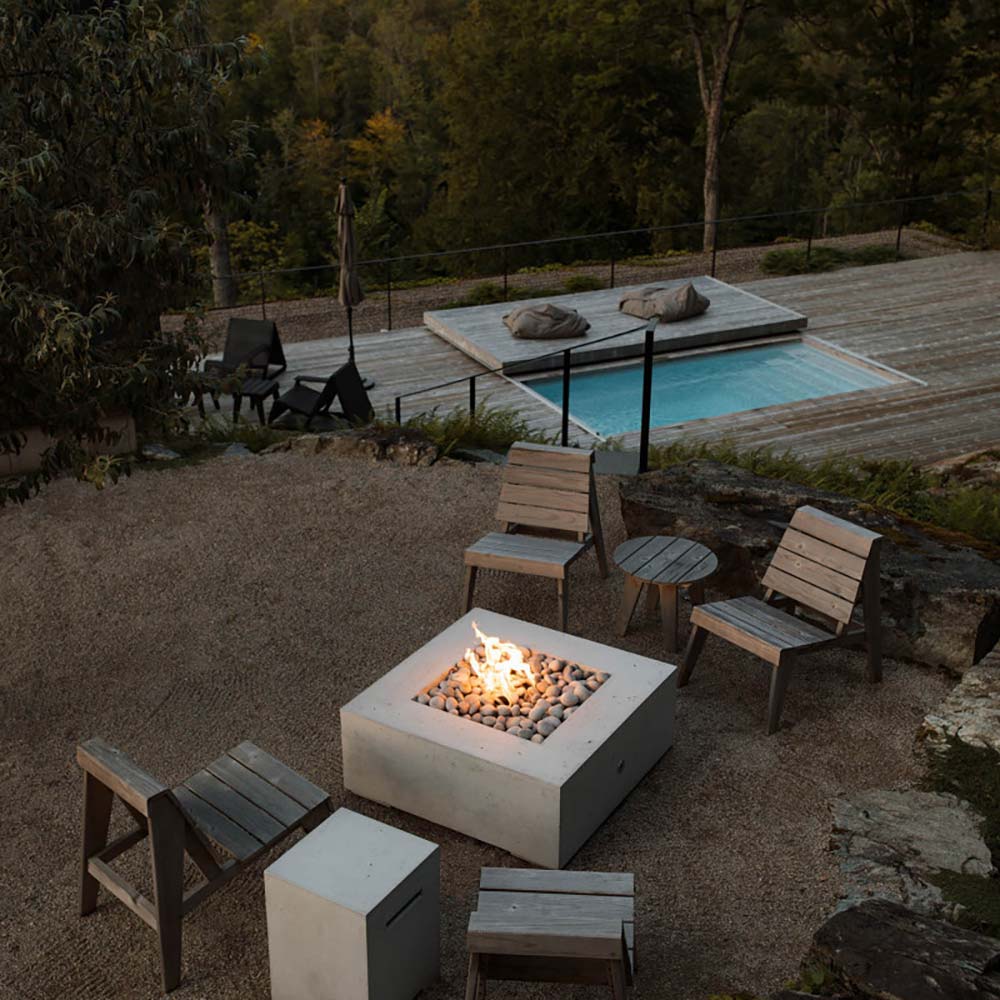 Square concrete gas fire pit with lit fire in shallow stone bed