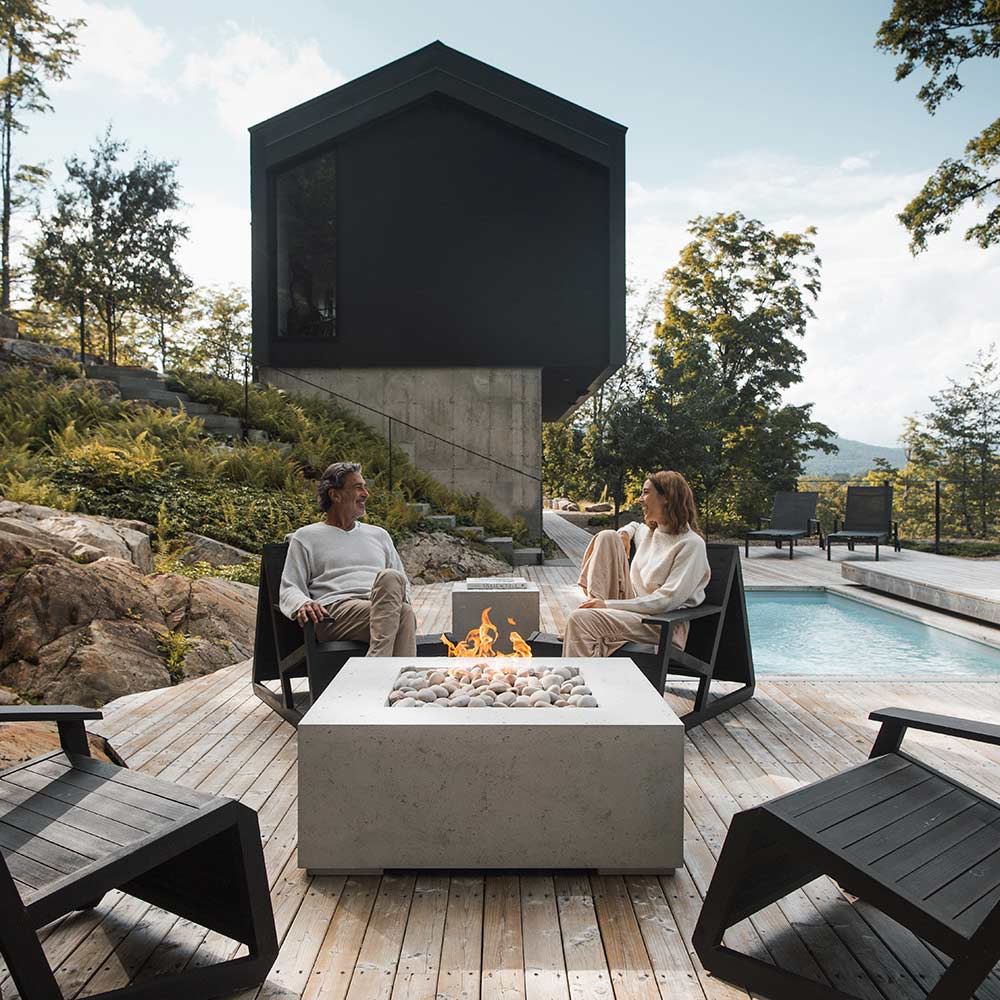 Square concrete gas fire pit with flames and gray stones on patio