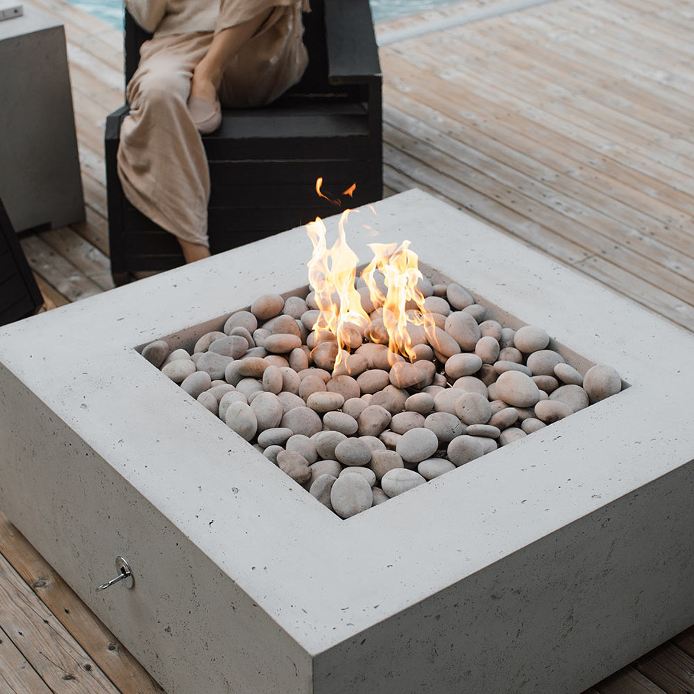 Square concrete gas fire pit with flames and gray round stones