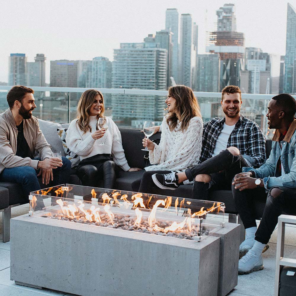 Rectangular concrete gas fire pit with flames and stone fire media on rooftop patio