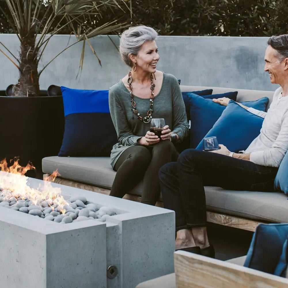 Concrete gas fire pit with flames near patio couches and pillows