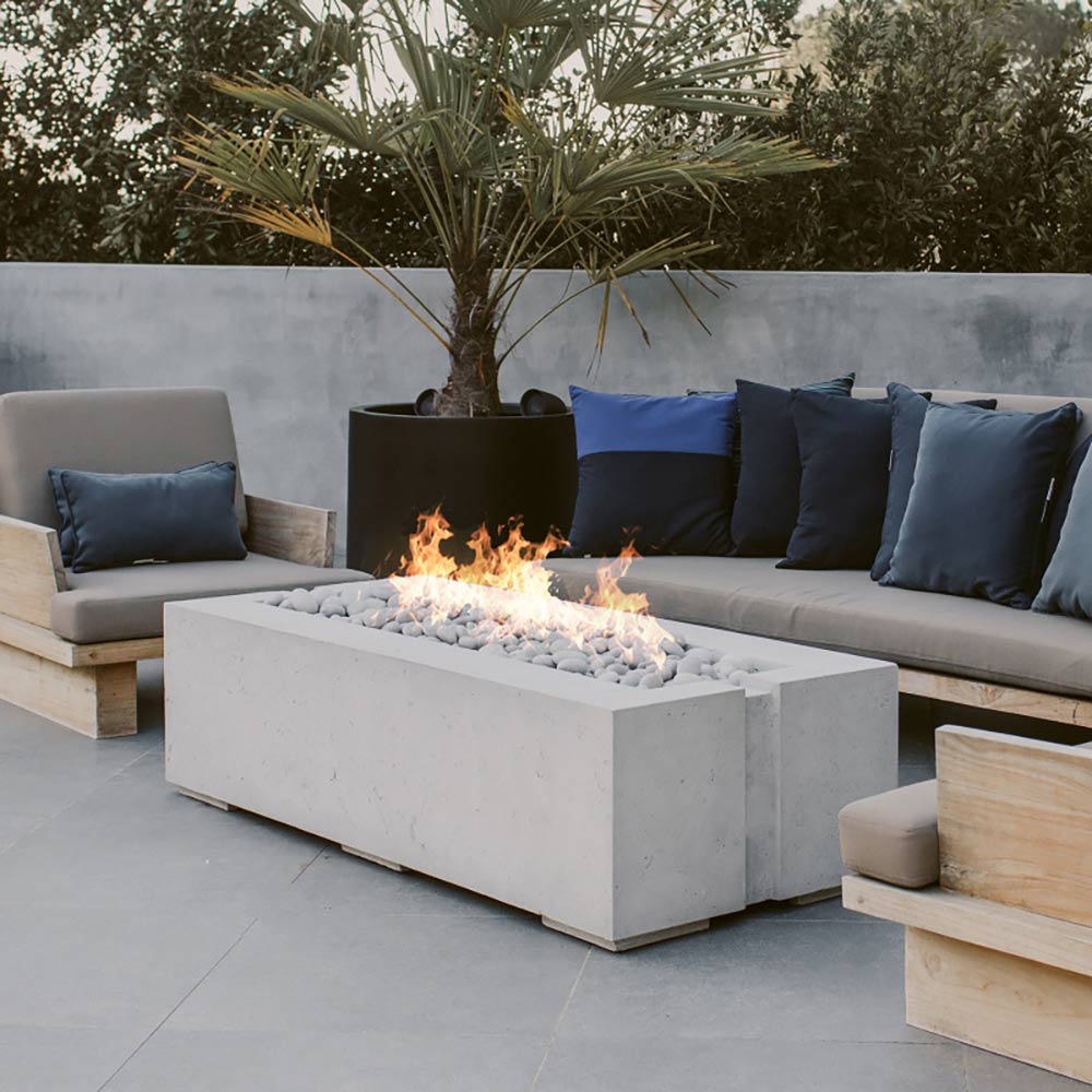 Concrete gas fire pit with flames and white rocks in outdoor lounge