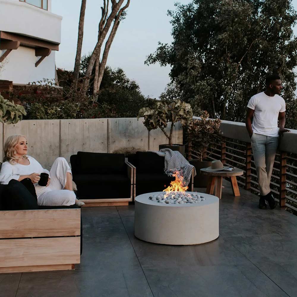 Light gray round concrete gas fire pit with visible flames and stone surround