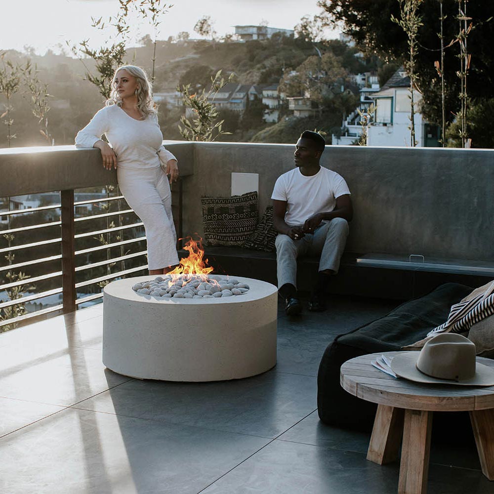 Light gray round concrete gas fire pit with flames over smooth stones