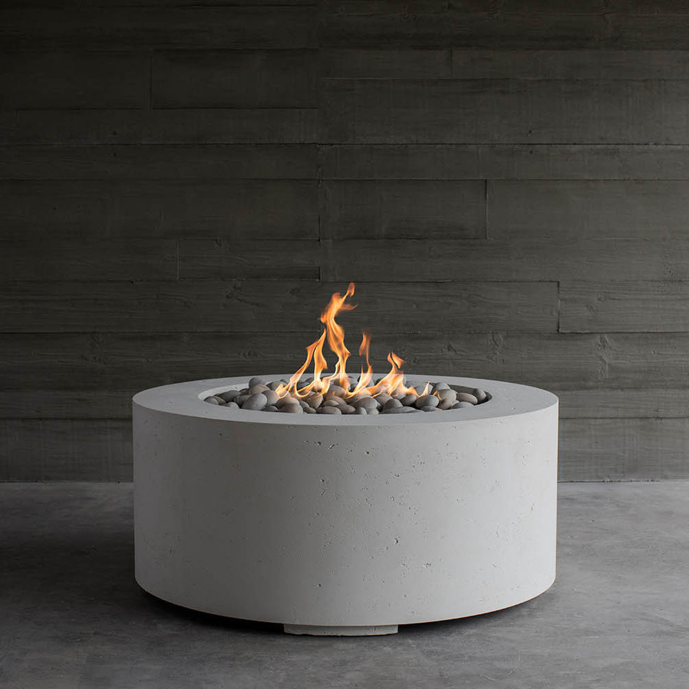 Light gray round concrete gas fire pit with flames in a stone-filled bowl