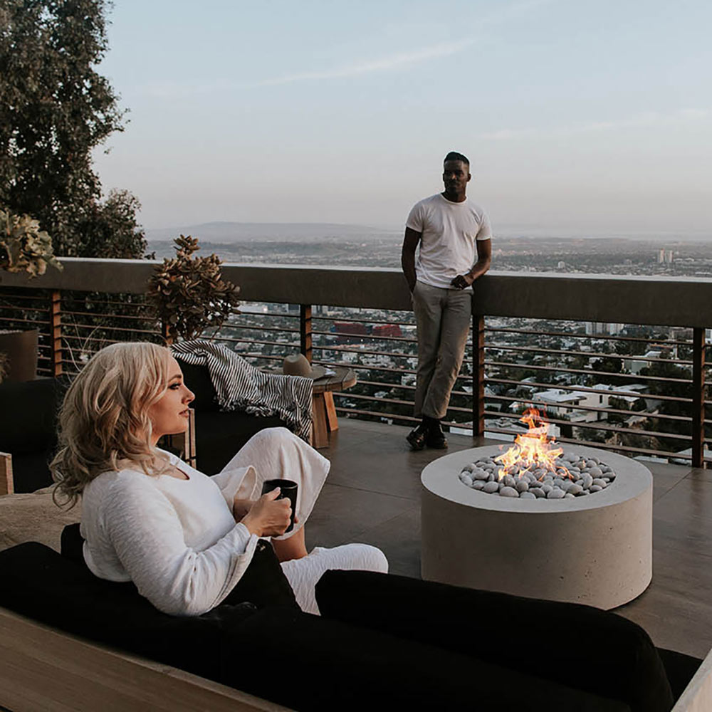 Light gray round concrete gas fire pit with flames, viewed from the side