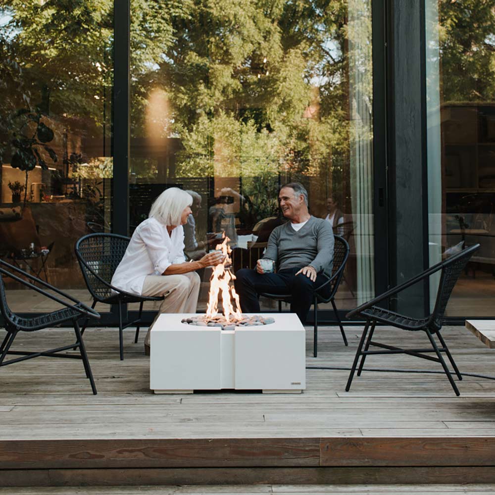 Square concrete gas fire pit with flame and stone filler on a patio table