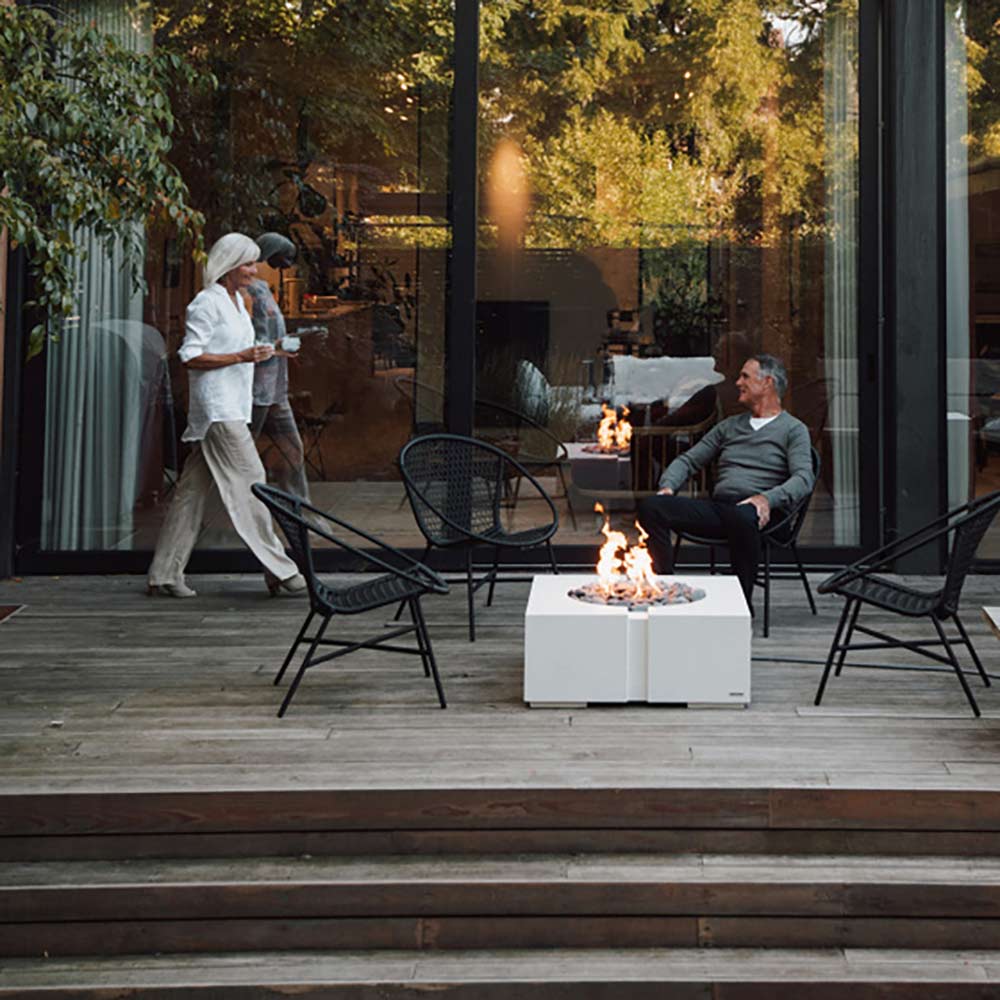 Square concrete gas fire pit with flame and river stones on an outdoor deck