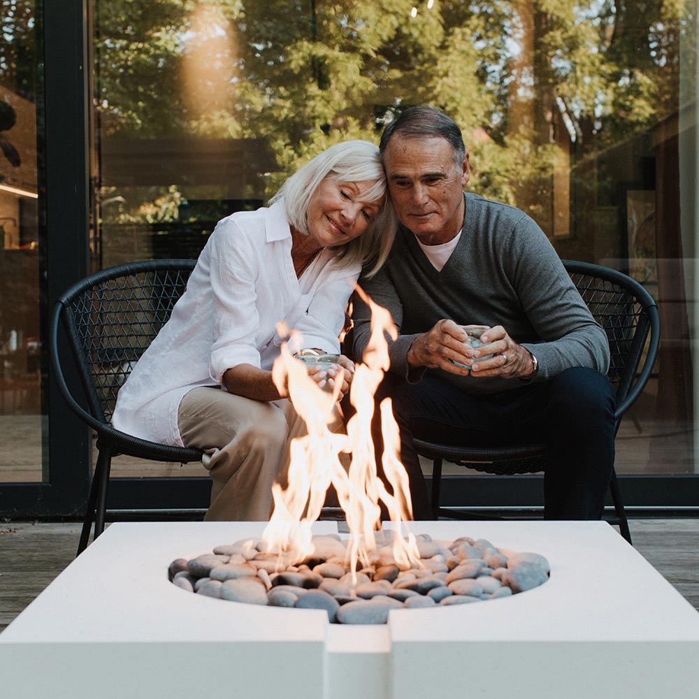 Square concrete gas fire pit top with bright flame and gray river rocks